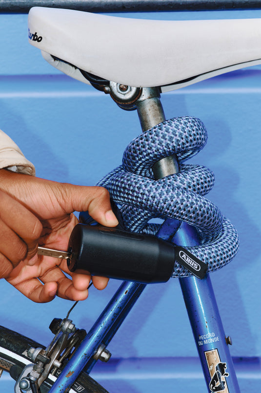 Person using a bike lock on a bicycle with a blue background