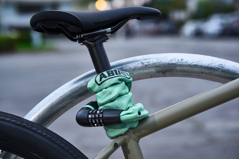 Load image into Gallery viewer, Bicycle locked with a green ABUS lock on a blurred street background #color_sage green
