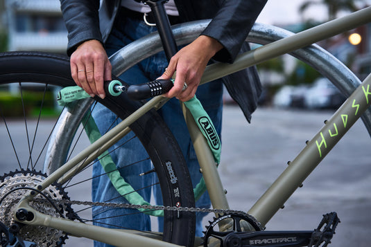 Person holding a green bike lock on a bicycle with 'Hudski branding.