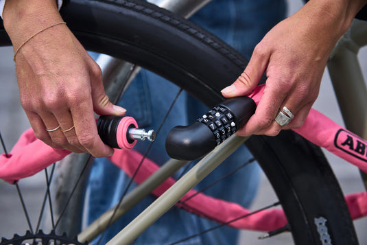 Person adjusting a bike lock on a pink bicycle.