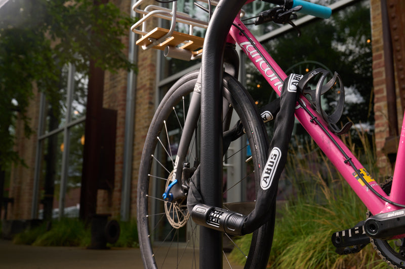 Load image into Gallery viewer, Pink bicycle locked to a bike rack with a building in the background #color_black

