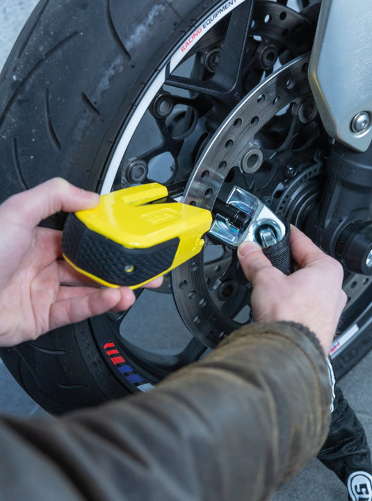 Person using a yellow tool on a motorcycle wheel