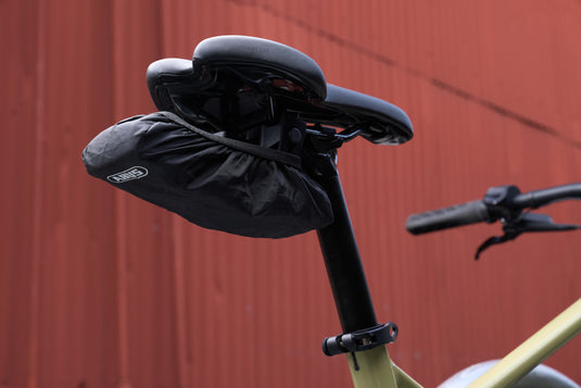 Close-up of a bicycle seat with a Bordo 6000K Saddlefix mounted with raincap against a blurred red background